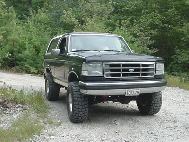 Lifted dark green Ford Bronco with white top on a gravel road, front three-quarter view