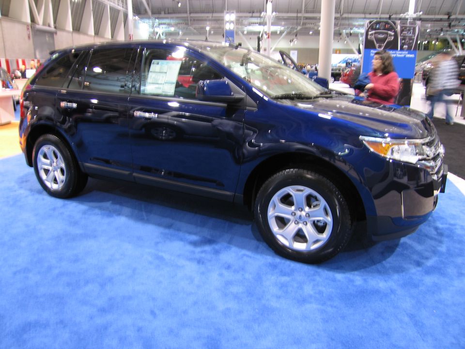 Blue SUV on a blue carpet, likely at a car show. Window sticker visible