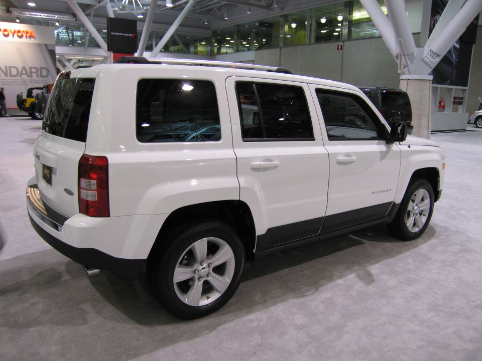 White Jeep Patriot parked indoors, side view. 'PATRIOT' text visible on the lower door