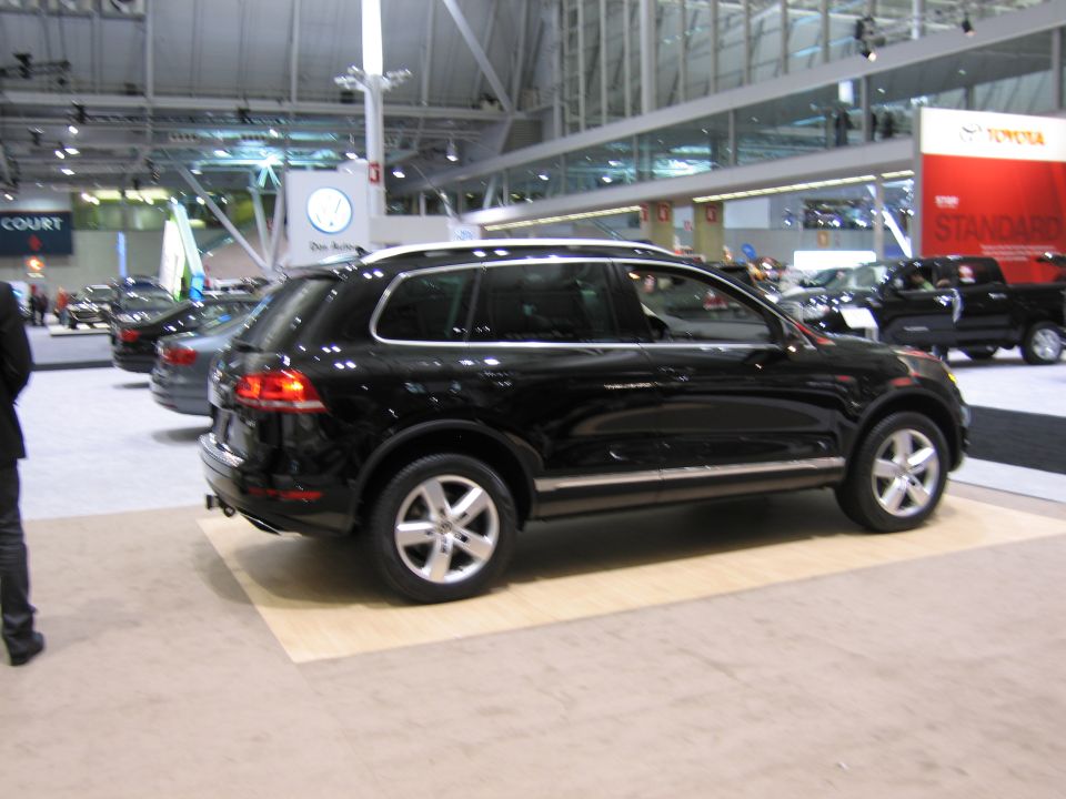 Black SUV on display at an auto show, with other vehicles and booths in the background