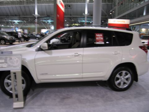 1991 Ford LTD Crown Victoria - A white Toyota RAV4 Limited SUV is displayed indoors, likely at a car show or dealership, with other vehicles visible in the background.