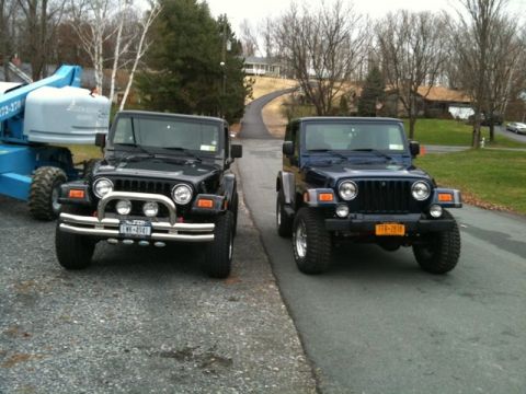 1972 Ford Ranchero - Two Jeep Wrangler TJs parked front-to-camera side by side on a paved driveway, the black one on the left wearing a polished chrome brush gu…