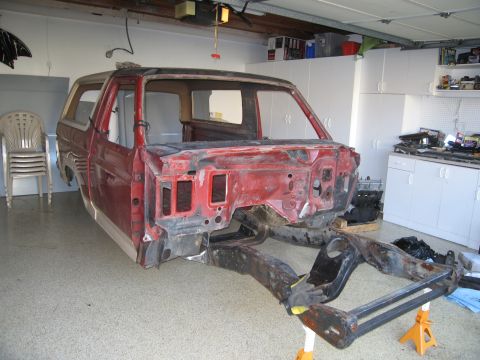 1986 Ford Bronco - Disassembled red Ford Bronco body and frame are visible in a garage, undergoing restoration.