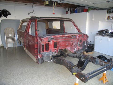 1986 Ford Bronco - The body of a red Ford Bronco is shown separated from its chassis, undergoing restoration in a garage.