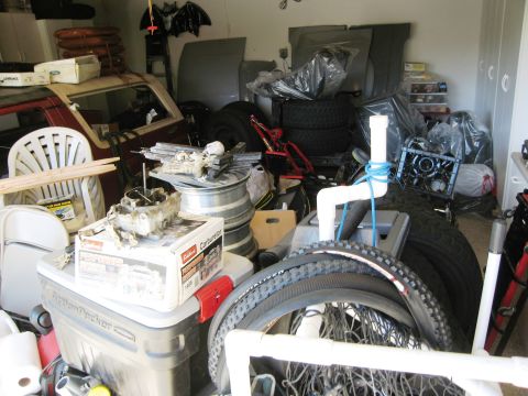 1986 Ford Bronco - A 1980s Ford Bronco is partially visible in a garage filled with car parts and tires.