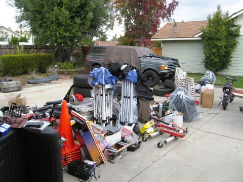 1986 Ford Bronco - A gray Ford Bronco is partially covered by a tarp, surrounded by various items in a driveway.