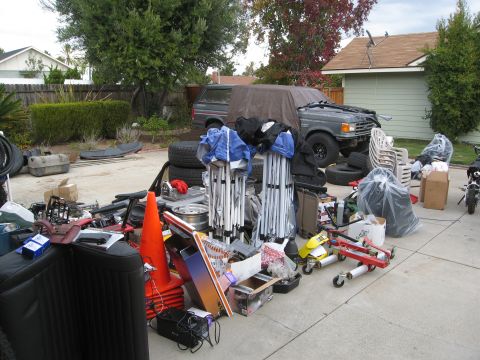 1986 Ford Bronco - A 1987 Ford Bronco is partially covered by a tarp, surrounded by various items in a cluttered driveway.