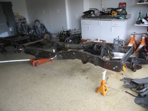 1986 Ford Bronco - A vehicle frame is supported by jack stands in a garage, with an engine and other parts visible in the background.