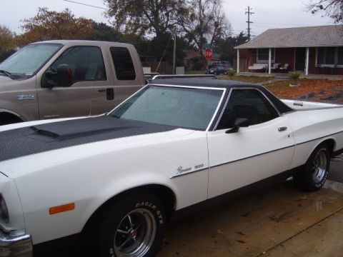 1973 Ford Ranchero - A white 1973 Ford Ranchero with a black hood scoop and vinyl top is parked next to a tan pickup truck.