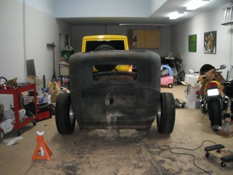 1986 Ford Bronco - A black car body sits in a garage with a yellow SUV visible behind it, along with a motorcycle and various tools.