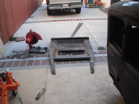 1986 Ford Bronco - Car frame and parts laid out on a driveway next to a chop saw.