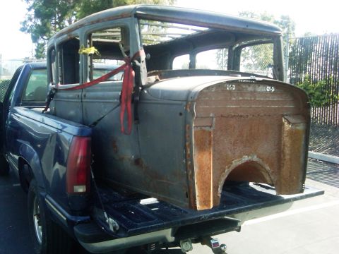 1986 Ford Bronco - A vintage car body, heavily rusted, is secured with straps in the bed of a pickup truck.