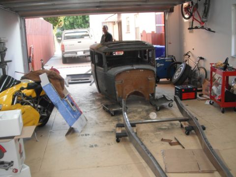 1986 Ford Bronco - A vintage car body and frame are in a garage, with a truck visible outside and a motorcycle parked nearby.