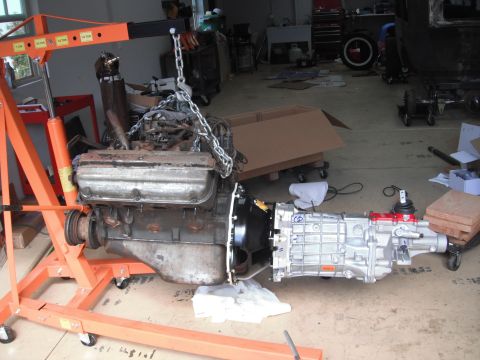 1986 Ford Bronco - Engine and transmission assembly suspended by an orange engine hoist in a garage setting.
