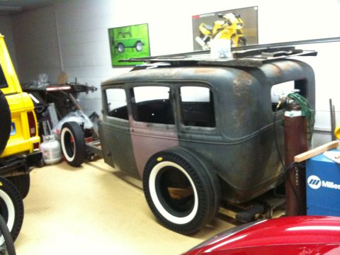 1986 Ford Bronco - A vintage sedan body sits in a workshop, awaiting restoration, with a yellow SUV visible to its left.