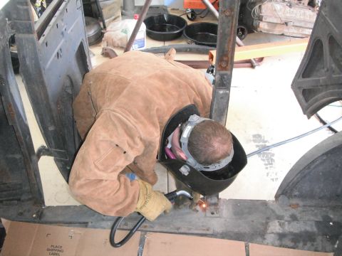 1986 Ford Bronco - A person is welding on the chassis of a vehicle, likely undergoing restoration.