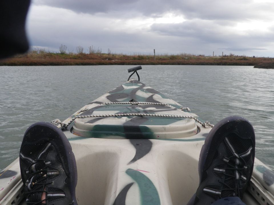 Kayak with camouflage pattern on water, view from inside looking forward, feet visible