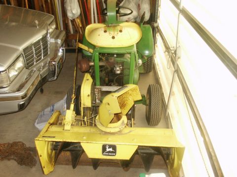 1966 Ford Bronco - A yellow John Deere tractor equipped with a snow blower attachment is parked next to a silver car in a garage.