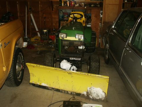 1966 Ford Bronco - Lawn tractor with a snow plow in a garage, next to a Ford Bronco and a sedan.