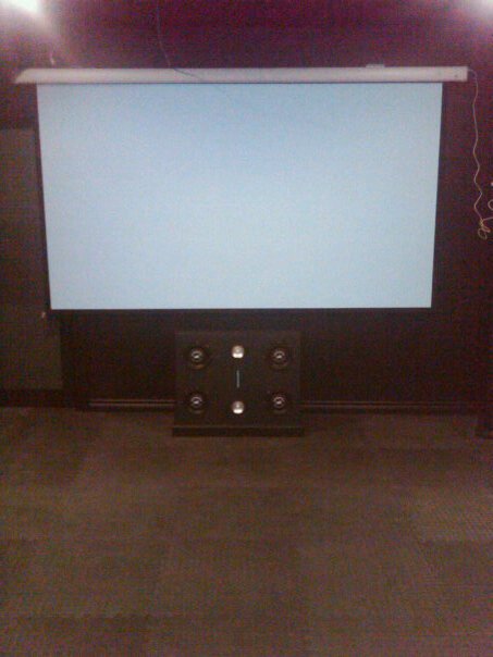 1987 Ford Bronco - A projector screen hangs above a set of speakers in a dimly lit room, with the Supermotors.net logo visible at the bottom right.