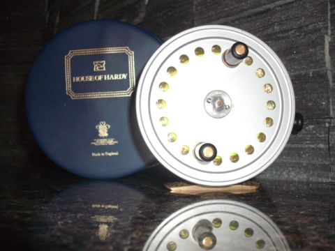 1990 Ford Bronco - A silver fishing reel is shown next to its blue House of Hardy case, which reads 'Made in England'.
