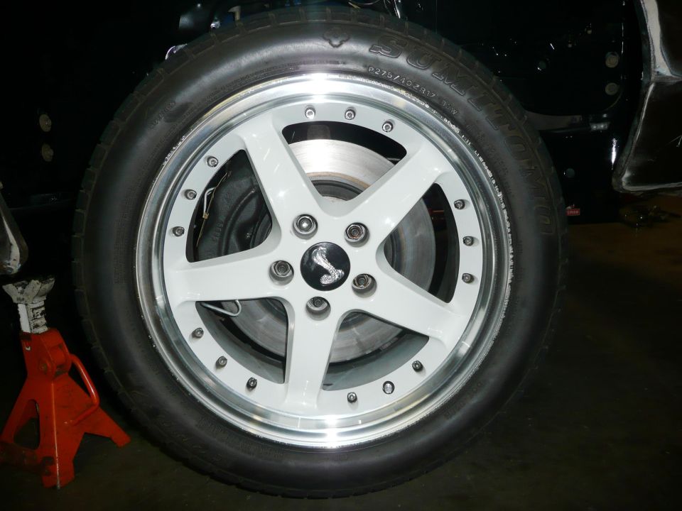 White five-spoke wheel with Cobra center cap and Sumitomo P275/40ZR17 tire, car on red jack stand