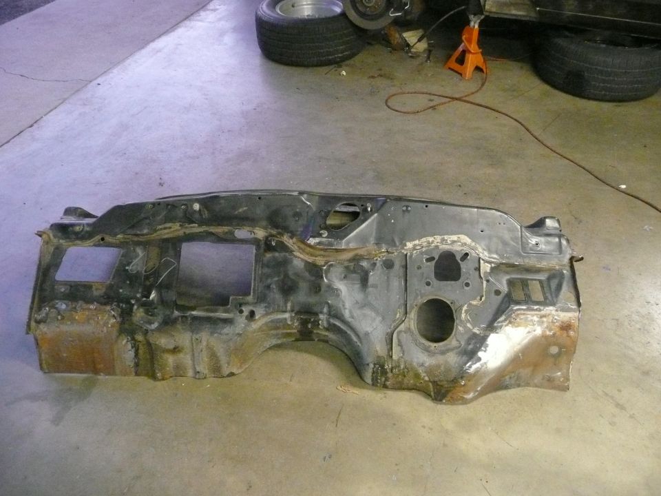 Rusty automotive firewall sheet metal panel laid on a garage floor