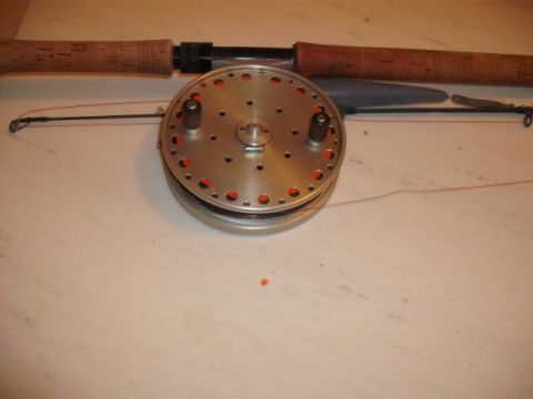1990 Ford Bronco - A fishing rod and reel are laid out on a light-colored surface. The reel has a distinctive perforated design.