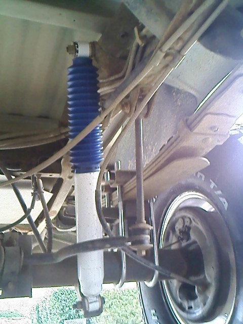 1995 Ford F-150 - This image shows the rear suspension components of a truck, including a shock absorber and leaf springs, along with a portion of the tire.