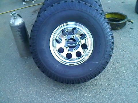 1995 Ford F-150 - A collection of tires and wheels are piled on the ground next to a metal cylinder and an oil drain pan.
