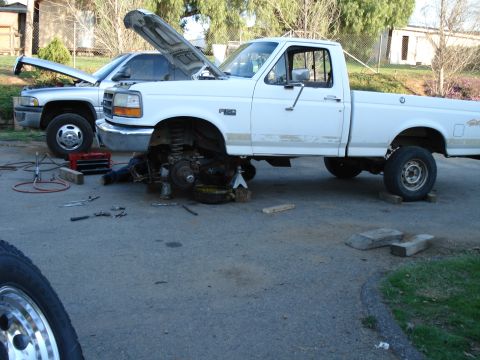 1995 Ford F-150 - A 1995 Ford F-150 is being worked on, with its front wheel off and hood open, while another truck sits nearby.