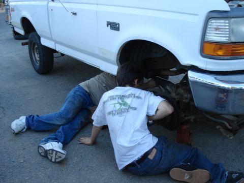 1995 Ford F-150 - Two people work on the front wheel assembly of a 1995 Ford F-150 truck.