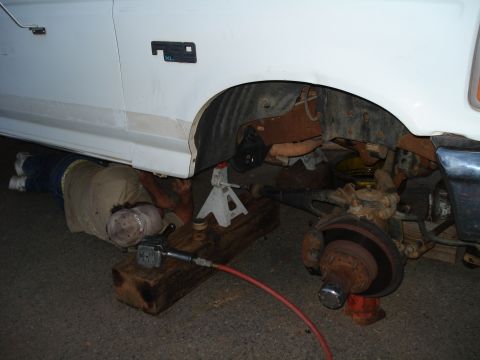 1995 Ford F-150 - A mechanic works on the front suspension of a white truck, which appears to be a 1995 Ford F-150.