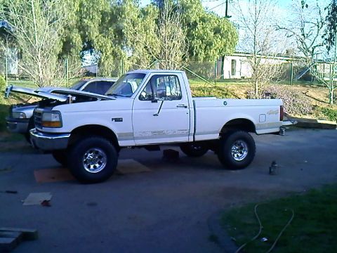 1995 Ford F-150 - White 1990s Ford F-150 regular-cab on a lift kit and chrome wheels, hood raised on a residential driveway.