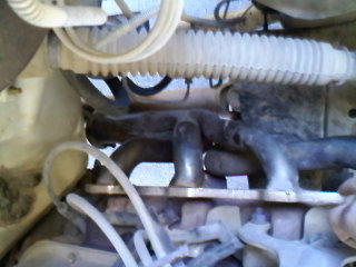 1995 Ford F-150 - Close-up of an exhaust manifold and associated hoses, with a SuperMotors watermark visible.