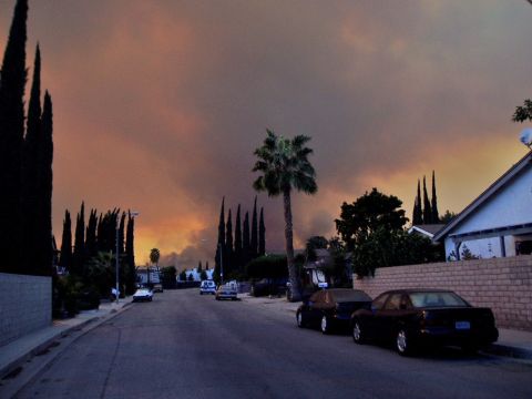 1993 Ford Taurus - Smoke fills the sky over a suburban street with parked cars and palm trees.