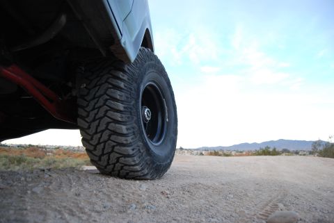 1982 Ford Bronco - A close-up view of a vehicle's tire and suspension system on a dusty, outdoor terrain.