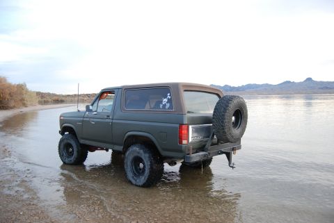 1982 Ford Bronco - This 1980s Ford Bronco is parked on a wet, sandy shore with a body of water and distant mountains in the background.