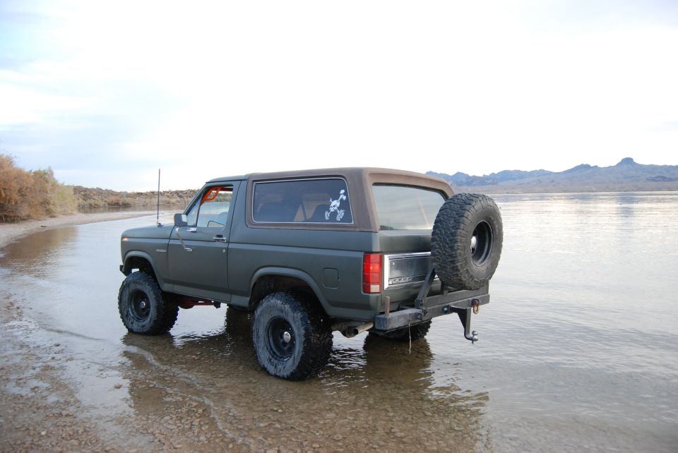 Dark green Ford Bronco with spare tire on back parked near water