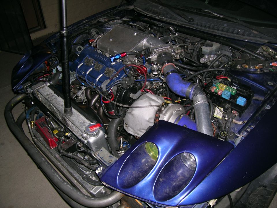Engine bay with turbo, intercooler, and custom intake manifold. Blue paint on fender and headlight housing