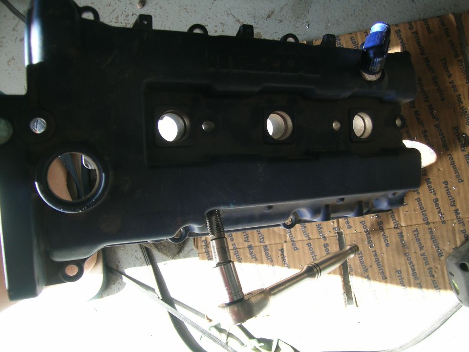 Black engine valve cover with bolt and socket wrench on cardboard