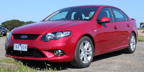 2010 Ford Falcon - A red sedan is parked on a dirt road with a blue sky overhead and some grass in the foreground.