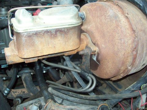 1985 Ford Bronco - Close-up of a brake master cylinder and booster assembly, showing rusted metal and various hoses and wires.