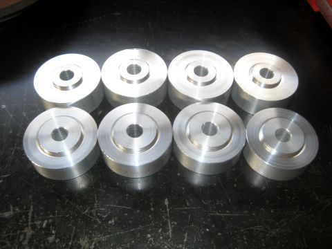 1996 Ford Bronco - Eight freshly machined aluminum spacers or body-mount pucks arranged in two rows on a scratched black bench top, each turned with a stepped…