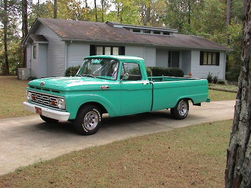 Teal-green classic Ford F-100 pickup parked in a driveway in front of a gray house