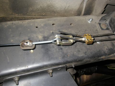 1990 Ford Bronco - Close-up under a vehicle showing a parking brake cable equalizer setup on a painted frame rail: a threaded adjuster rod through an eye bolt…