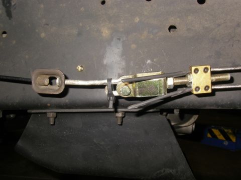 1990 Ford Bronco - Underbody view of a parking brake cable equalizer setup, with a yellow zinc-plated clevis and adjuster nut joining a threaded rod to a gold…