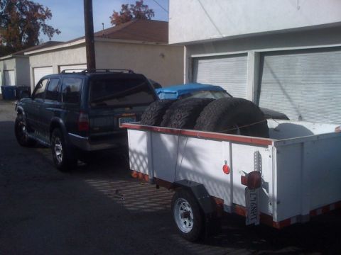 1968 Ford Mustang - A dark SUV is seen towing a trailer loaded with four tires. The SUV's license plate is visible.
