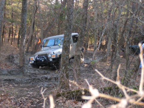 2005 Jeep Wrangler - A Jeep Wrangler navigates a challenging muddy trail surrounded by trees.