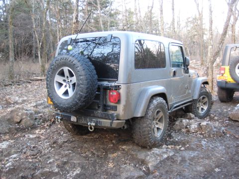 2005 Jeep Wrangler - A gray 2005 Jeep Wrangler navigates a rocky, muddy off-road trail with another Jeep visible in the background.